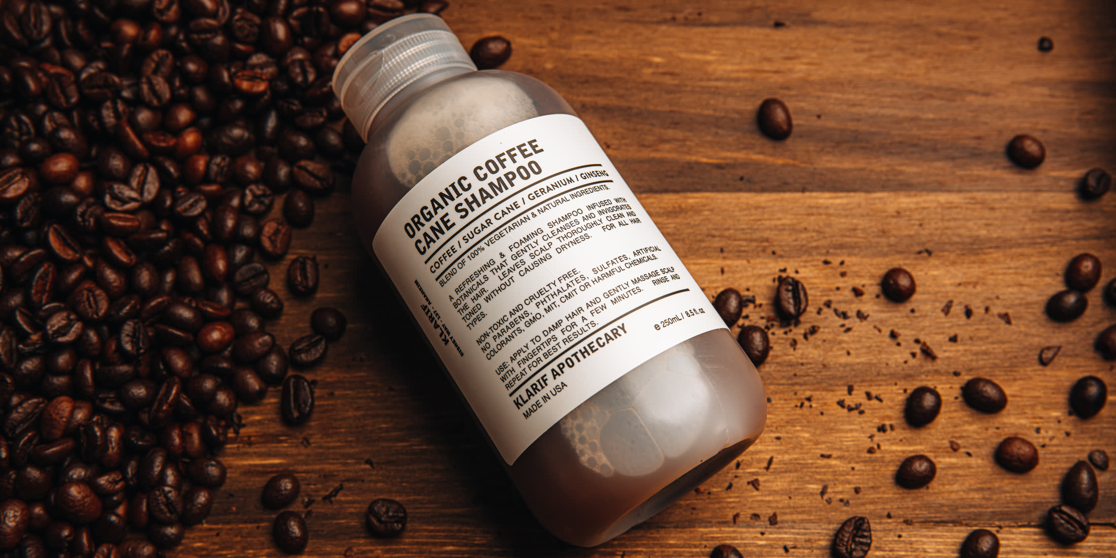 Klarif organic coffee cane shampoo bottle on dark wood with spilled coffee beans